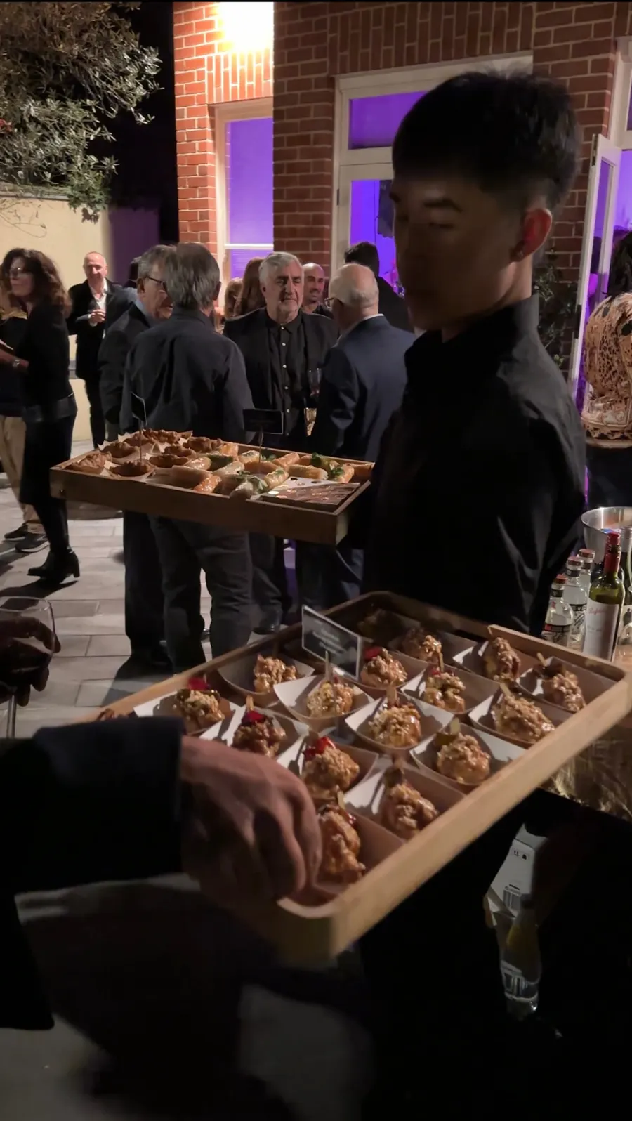 A Mister Minh waiter carrying trays of canapés at an evening garden event